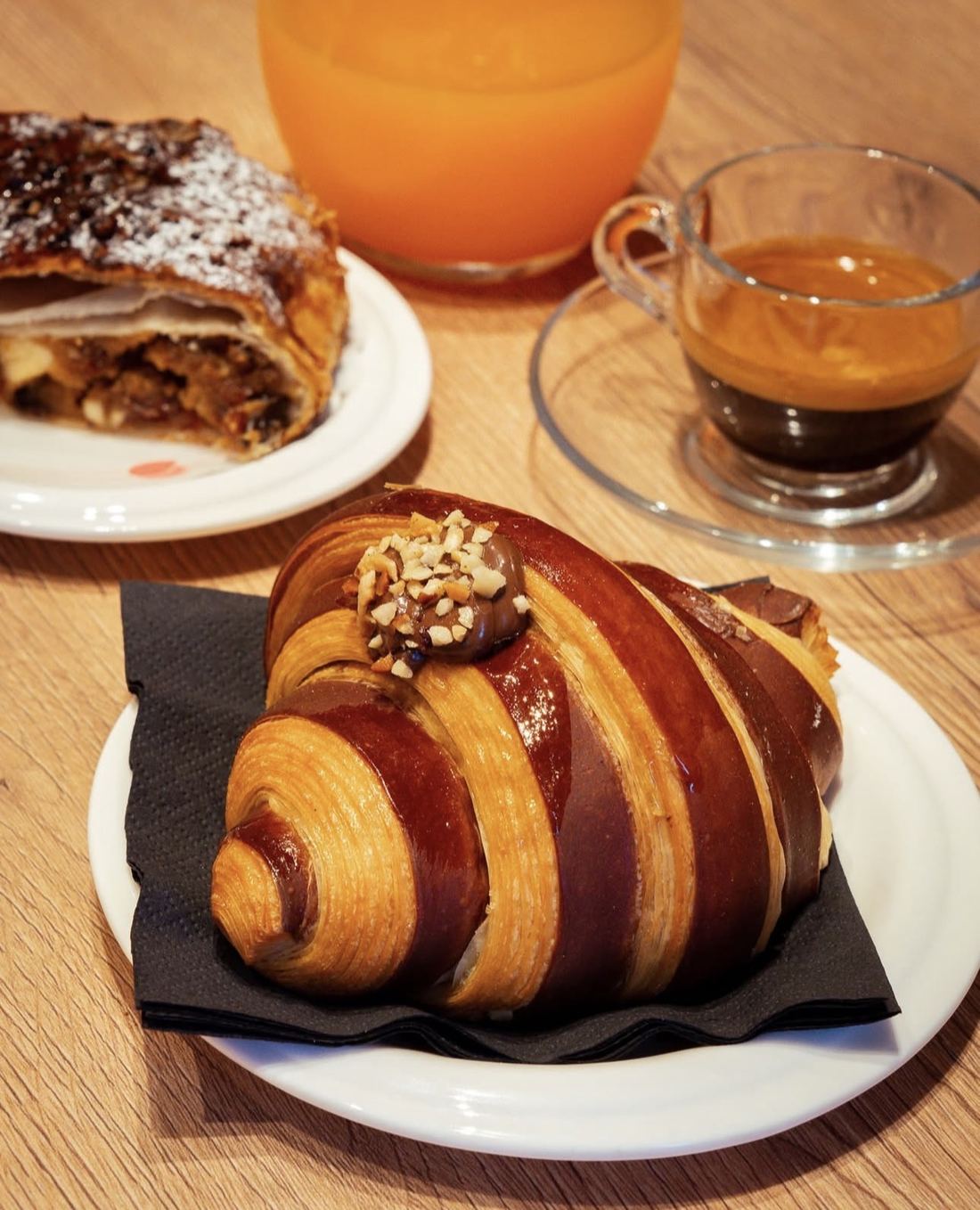 Colazione al banco: un croissant lucido con crema alle nocciole, una fetta di strudel, un espresso e una spremuta