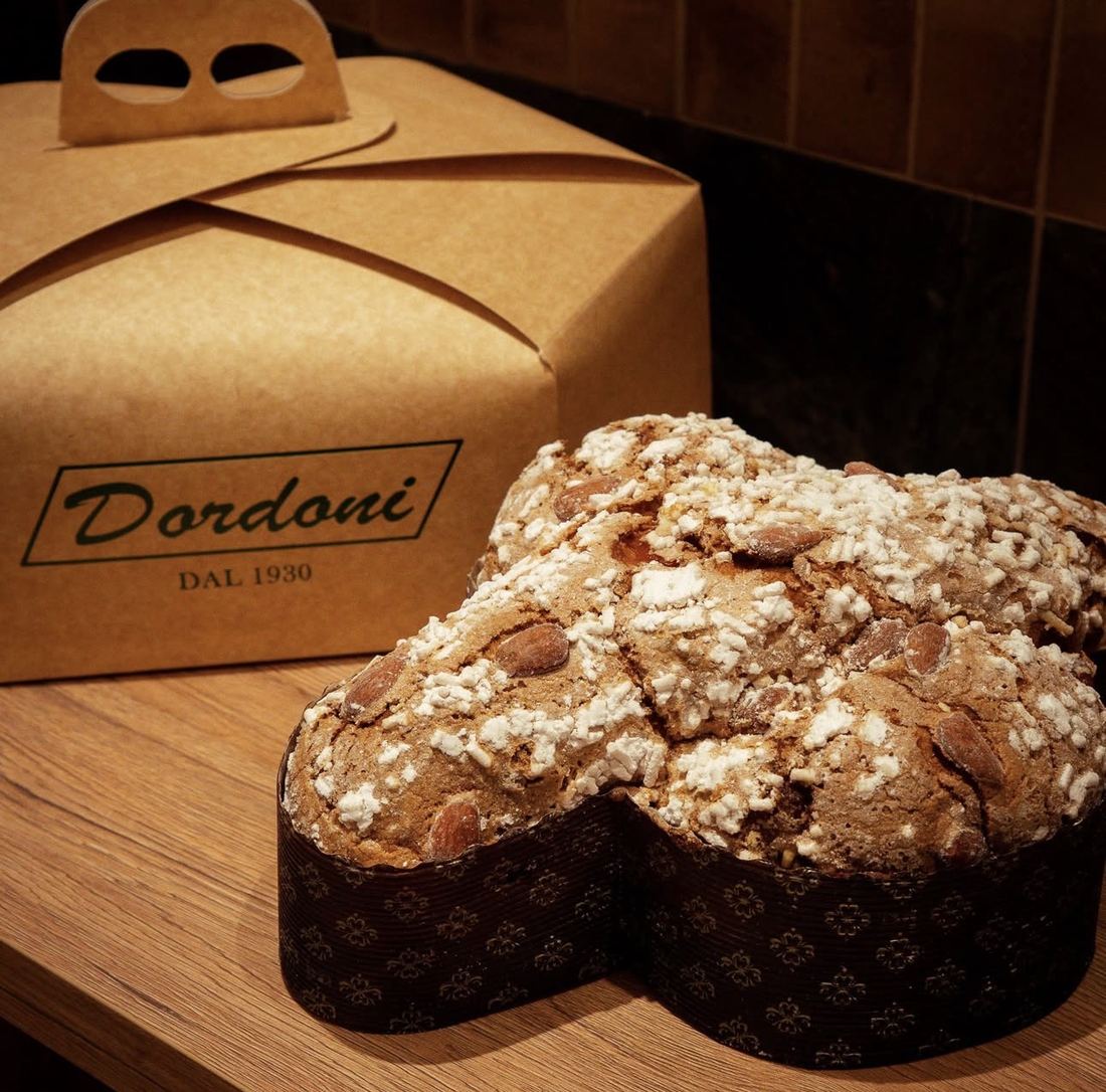 Una colomba glassata con mandorle e granella di zucchero accanto a una scatola Dordoni dal 1930
