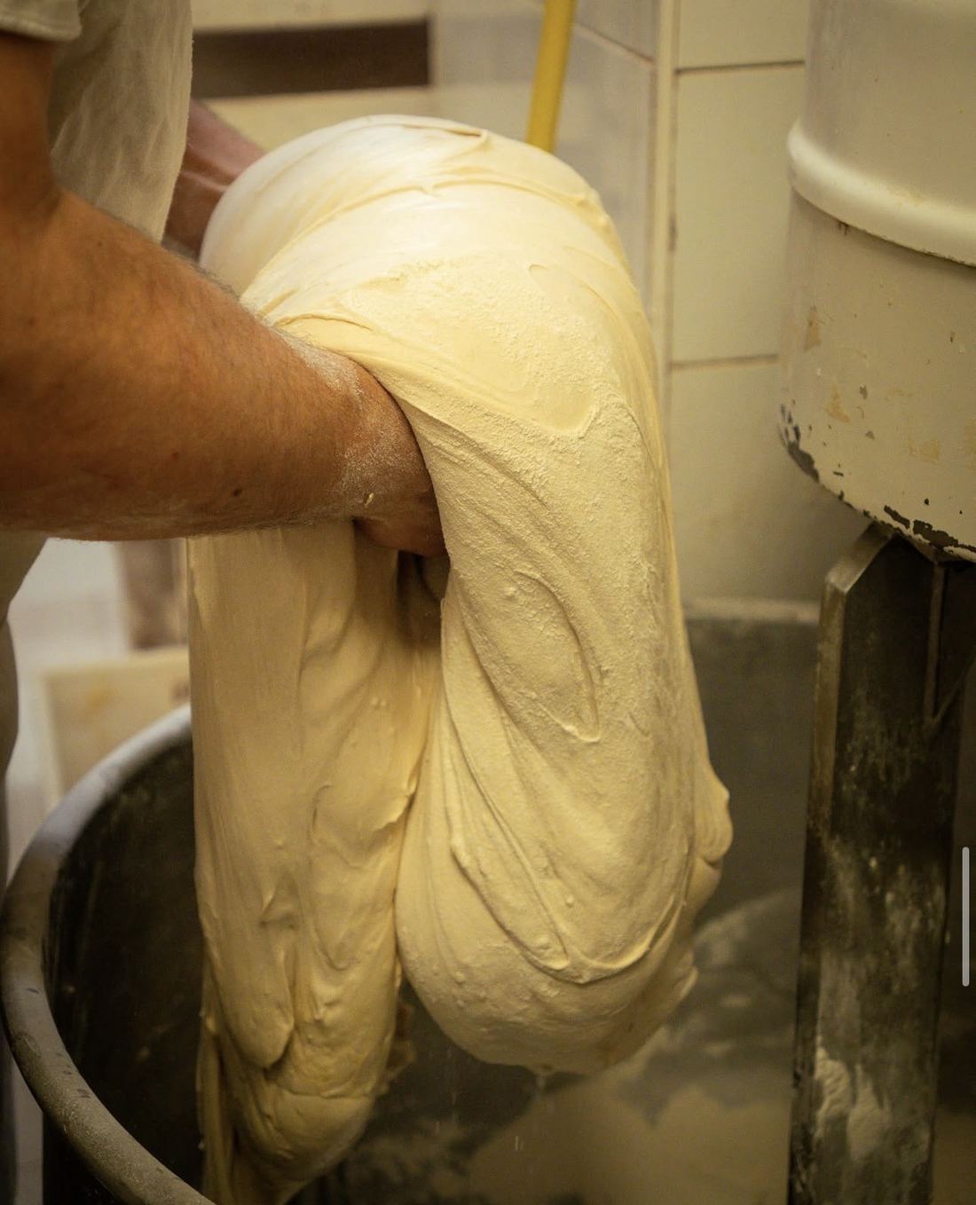 Un panettiere solleva a mano un grande impasto morbido dall’impastatrice
