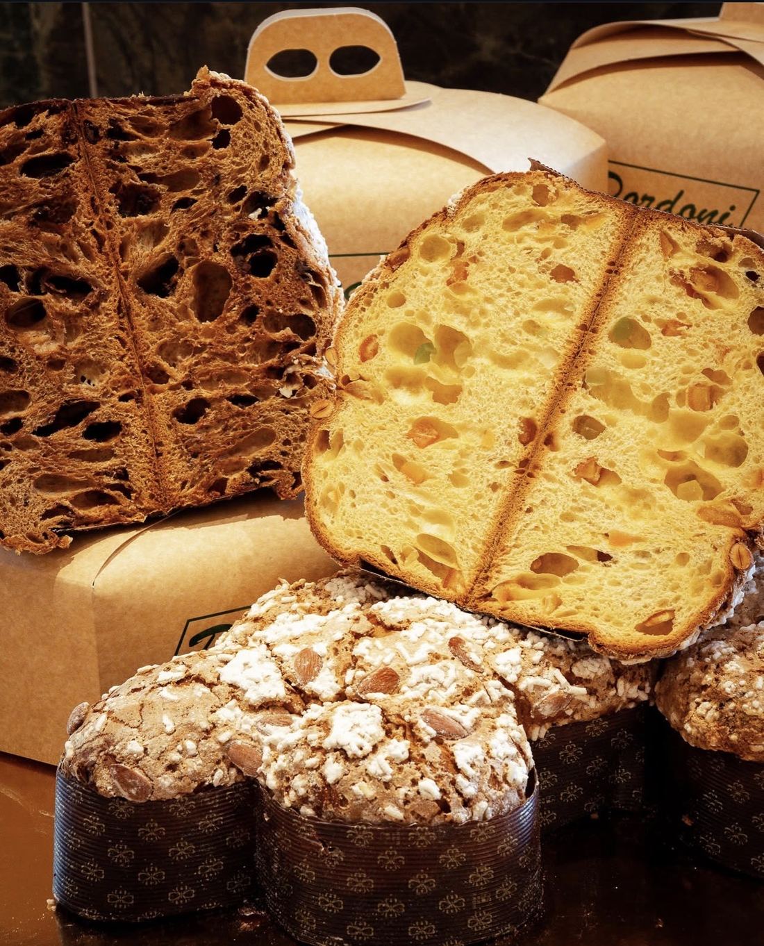 Panettoni tagliati a metà e colombe glassate in primo piano, davanti alle scatole Dordoni
